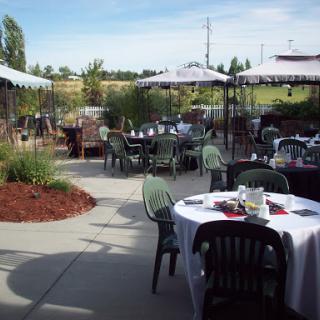 A serene outdoor dining area featuring tables shaded by umbrellas, surrounded by lush greenery.