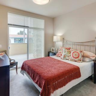 A cozy bedroom with a decorated bed, bedside lamp, and sliding glass door leading to a balcony.