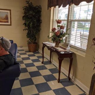 A cozy waiting room with checkered flooring, a window letting in natural light, and a decorative table with flowers.