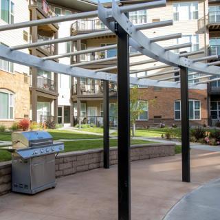 Outdoor patio area with a pergola and grill at an apartment complex.