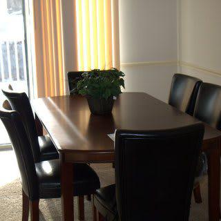 A dining room with a wooden table and six chairs, featuring a potted plant centerpiece.