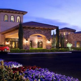 A luxury hotel building with elegant architecture and beautifully landscaped flower beds illuminated during the evening.