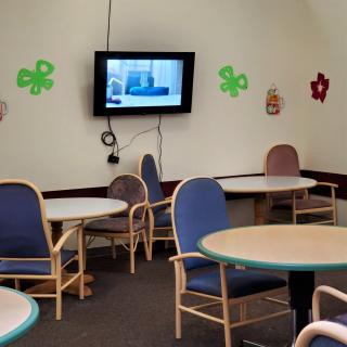 A common area with tables and chairs, featuring a television and wall decorations.