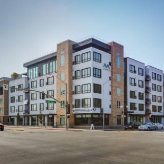 A modern apartment building located on a street corner in an urban area.