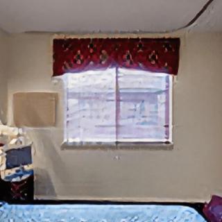 A cozy hotel room featuring a bed, a window with red curtains, and a bedside lamp.