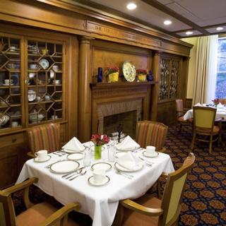A elegantly set dining table in a traditional dining room with a fireplace and decorative wooden cabinetry.