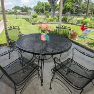 A patio set consisting of a round metal table with six matching chairs, surrounded by a garden view.