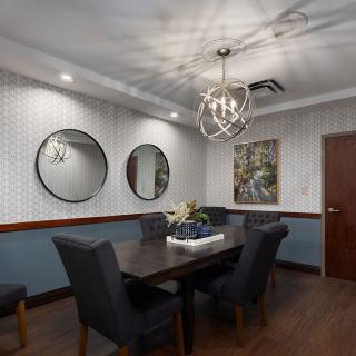 A modern dining room featuring a sleek table and upholstered chairs, with decorative mirrors and artwork adorning the walls.