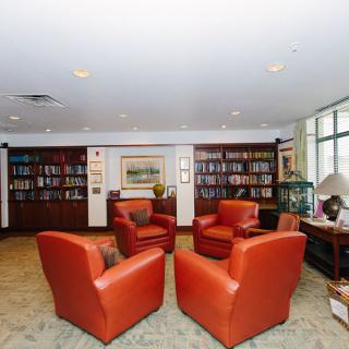 A cozy library room featuring a seating area with red chairs and walls lined with bookshelves.