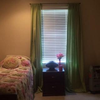 A cozy bedroom featuring a bed with floral bedding, green curtains, and a nightstand with a lamp.