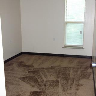 An empty room with carpet flooring and a single window.