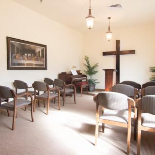 A small chapel interior with rows of chairs, an organ, and a cross on the wall.