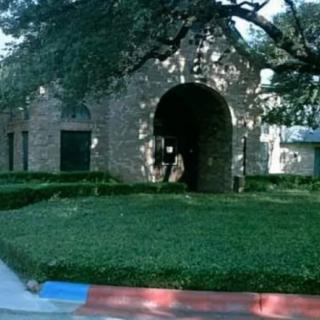 A brick building with an arched entrance surrounded by trees and a well-manicured lawn.
