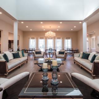 A spacious living room with elegant furniture and a chandelier, leading into a dining area.