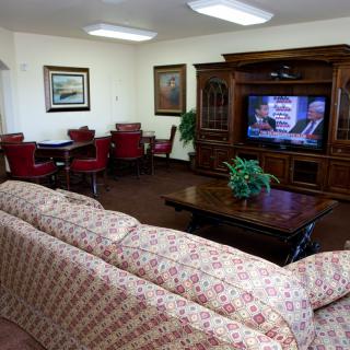 A cozy living room featuring a floral sofa, a wooden entertainment center with a television, and a set of red chairs around a small table.