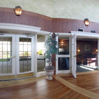 A spacious lobby with glass doors, warm lighting, and wooden flooring.