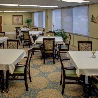 An empty dining room with tables covered in white tablecloths, surrounded by chairs and decorated with indoor plants.