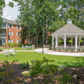 A serene garden area with a gazebo, surrounded by trees and a nearby building.