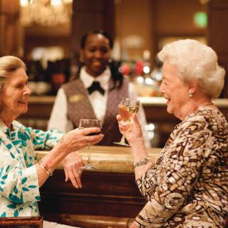 Two elderly women enjoy a toast at a bar, sharing laughter in a warm and social setting.