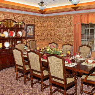 A classic dining room with a large table set for a meal, surrounded by upholstered chairs and decorated with a china cabinet in the background.