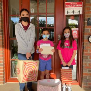 Three people standing in front of a door, wearing masks and holding shopping bags.