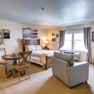 A cozy studio apartment features a comfortable bed, a small dining area, and ample natural light.