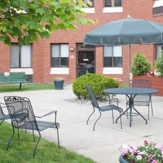 A peaceful outdoor patio area with seating and a large umbrella near a brick building.