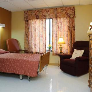 A well-furnished hospital room with a bed, armchair, and window providing natural light.