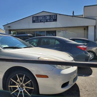 A white car parked in front of a building with a business sign.
