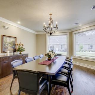A well-lit dining room featuring a large table with chairs, a chandelier, and large windows.