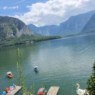 A serene view of a picturesque lake surrounded by mountains, dotted with colorful boats under a partly cloudy sky.