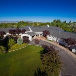 Aerial view of a large residential house with a winding driveway and lush green surroundings.