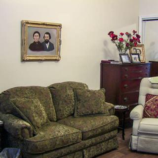 A cozy living room with a floral sofa, armchair, and decorative elements such as a painting and flowers.