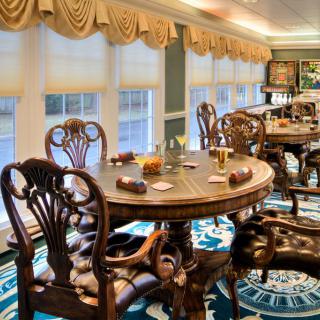 A luxurious dining room featuring a round wooden table and intricately designed chairs, complemented by elegant curtains and a patterned carpet.