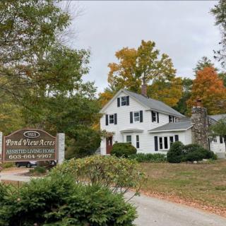 A charming white house surrounded by autumn foliage with a driveway leading up to it.