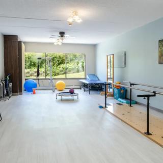 A spacious and bright rehabilitation room equipped with exercise equipment, mirrors, and ballet bars.