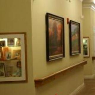 A hallway in an art gallery featuring framed paintings and illuminated display cases.