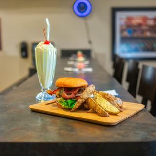 A delicious meal featuring a burger, fries, and a milkshake served on a wooden board in a restaurant setting.