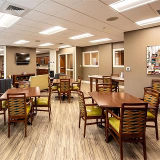 A well-lit dining area with multiple tables and chairs, featuring wooden flooring.