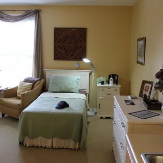 A cozy bedroom with a single bed, a lamp, and a comfortable chair by the window.