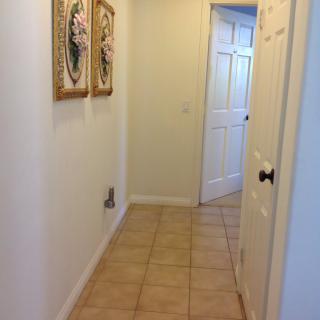 A tiled hallway with framed artwork on the walls leading to a doorway.
