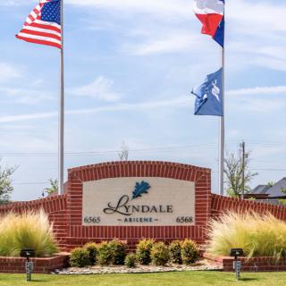 A brick entrance sign for Lindale surrounded by flags and landscaping.