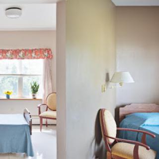 A cozy interior space featuring a bedroom with a bed and a living area with chairs, well-lit by natural light coming through a window.