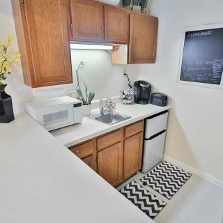 A compact kitchen with wooden cabinets, featuring a microwave, coffee maker, and a small chalkboard on the wall.