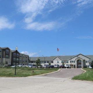 A large residential building with a driveway, surrounded by an open grassy area under a blue sky.