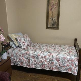 A cozy bedroom featuring a single bed with floral bedding, a nightstand, and a decorative painting on the wall.