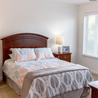 A cozy bedroom with a neatly made bed, a wooden nightstand, and a lamp by the window.