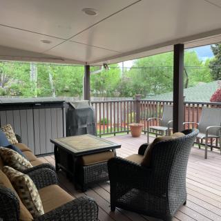 A cozy covered patio featuring comfortable outdoor seating, a hot tub, and lush greenery.