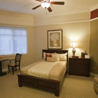 A cozy bedroom featuring a neatly made bed, wooden furniture, and a ceiling fan.