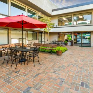 Outdoor patio area with tables, chairs, and a red umbrella on brick flooring.